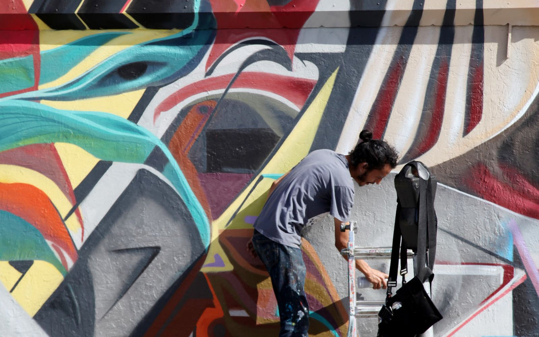 Artista che dipinge un murale con lo spray durante un live painting di street art
