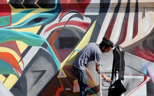 Artista che dipinge un murale con lo spray durante un live painting di street art